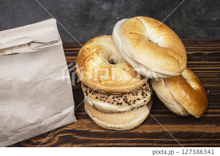 Closeup view of a heap of a collection of bagel breads with various kinds and a brown paper bag on a wooden board Closeup view of a heap of a collection of bagel breads with various kinds and a brown paper bag on a wooden board 127386341
