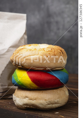 Closeup view of a pile of a collection of bagel breads with various kinds and a brown paper bag on a wooden board 127386345
