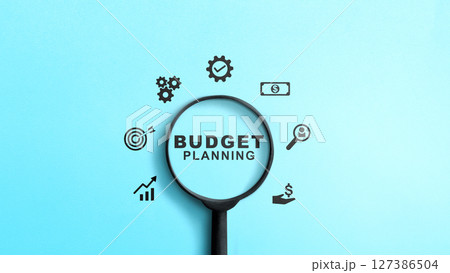 Magnifying glass showing text of budget planning with several finance icons on a colored background. Concept of budget planning 127386504