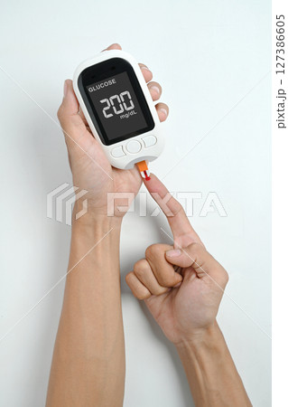 Human hand using a glucometer for checking blood sugar level isolated over a white background. Concept of diabetes or a healthy lifestyle Human hand using a glucometer for checking blood sugar level isolated over a white background. Concept of diabetes or a healthy lifestyle 127386605