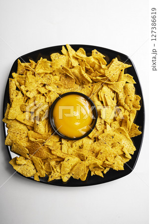 Nachos tortilla chips on the black plate with cheese sauce in a bowl on a white background. Food and snacks concept 127386619
