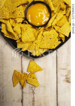 Nachos tortilla chips on the black plate with cheese sauce in a bowl on the table. Copy space. Food and snacks concept Nachos tortilla chips on the black plate with cheese sauce in a bowl on the table. Copy space. Food and snacks concept 127386631