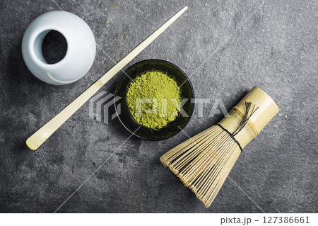 Matcha green tea powder in the black bowl and a traditional bamboo brush whisk with a spoon on a black table. Accessories for making matcha green tea. Top view 127386661