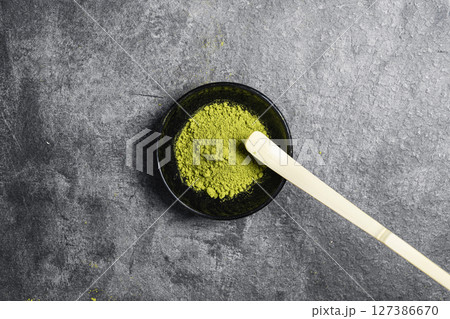 Matcha green tea powder in the black bowl and a traditional bamboo spoon or chashaku on a black table. Accessories for making matcha green tea. Copy space. Top view 127386670