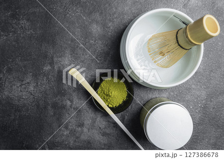 Matcha green tea powder in the black bowl with a wooden spoon and a traditional bamboo brush whisk in an empty bowl on a black table. Accessories for making matcha green tea. Top view 127386678