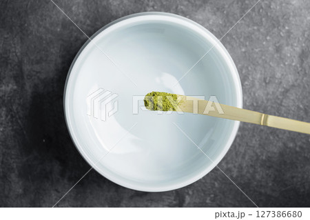 Traditional bamboo spoon or chashaku with matcha green tea powder pouring into an empty bowl on a black table. Accessories for making matcha green tea. Top view 127386680
