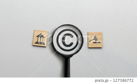 Magnifying glass with copyright logo and icon of law on wooden cubes. Concept of digital copyright and patent, intellectual assets and property, legal protection Magnifying glass with copyright logo and icon of law on wooden cubes. Concept of digital copyright and patent, intellectual assets and property, legal protection 127386772