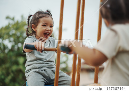 cheerful toddler girl playing on double swing with freind at outdoor playground cheerful toddler girl playing on double swing with freind at outdoor playground 127387164