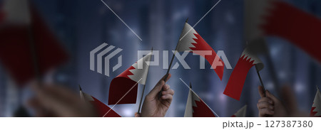 Bahrain flags in their hands on a blurred urban background Bahrain flags in their hands on a blurred urban background 127387380