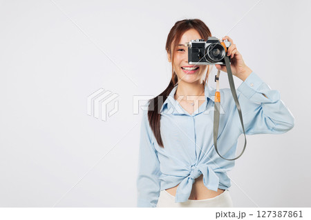 Camera carrying traveler taking shots with her images camera. Happy smiling Asian young woman enjoying photography adventure on summer holiday. isolated studio white background 127387861