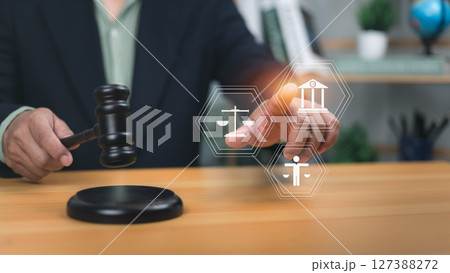 Human holding gavel pointing to holographic icons scales of justice, government building, and person. Symbolizes legal system, human rights, the rule of law for justice and regulatory compliance now. Human holding gavel pointing to holographic icons scales of justice, government building, and person. Symbolizes legal system, human rights, the rule of law for justice and regulatory compliance now. 127388272