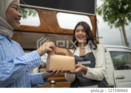 Indonesian southeast chinese asian female waiter serving food order to chinese muslim female customer. A small business on a truck Indonesian southeast chinese asian female waiter serving food order to chinese muslim female customer. A small business on a truck 127390668