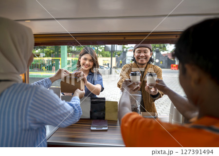 Indonesian southeast asian male and a Chinese muslim female in hijab couple baristas serving drinks and snacks to customers. A small business of a coffee shop or cafe on a truck Indonesian southeast asian male and a Chinese muslim female in hijab couple baristas serving drinks and snacks to customers. A small business of a coffee shop or cafe on a truck 127391494