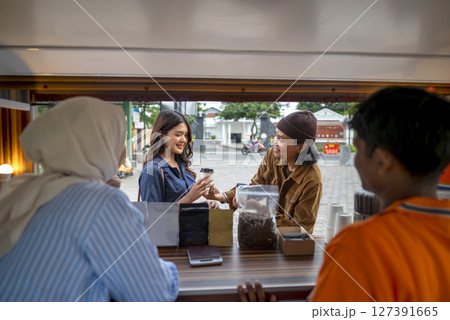 Indonesian southeast asian male and a Chinese muslim female in hijab couple baristas serving drinks and snacks to customers. A small business of a coffee shop or cafe on a truck Indonesian southeast asian male and a Chinese muslim female in hijab couple baristas serving drinks and snacks to customers. A small business of a coffee shop or cafe on a truck 127391665