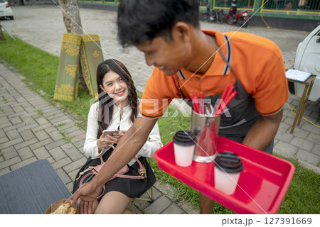 Indonesian southeast asian male barista serving a drink and food to the customer. A small business of a coffee shop or cafe on a truck 127391669