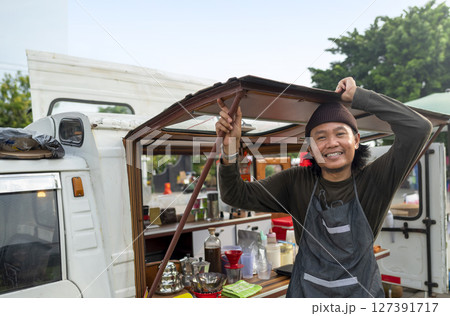 Indonesian southeast asian male barista standing with confidence in front of his coffee shop. A small business of a coffee shop or cafe on a truck Indonesian southeast asian male barista standing with confidence in front of his coffee shop. A small business of a coffee shop or cafe on a truck 127391717