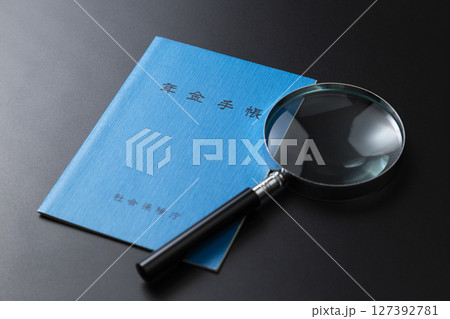 黒背景に年金手帳と虫眼鏡 127392781