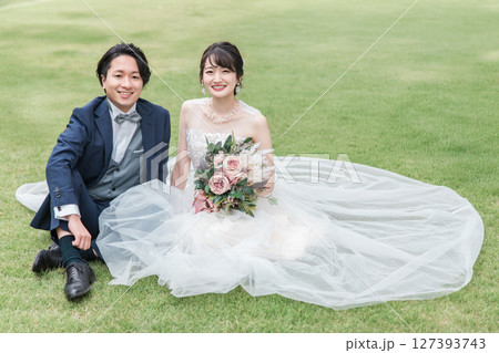 式場のガーデンの芝生に座るウェディングドレス姿の新婦と新郎(ウェディングフォト) 式場のガーデンの芝生に座るウェディングドレス姿の新婦と新郎(ウェディングフォト) 127393743
