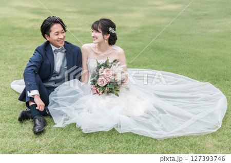 式場のガーデンの芝生に座るウェディングドレス姿の新婦と新郎（ウェディングフォト） 127393746