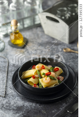 Paccheri pasta with shrimps, asparagus and chili pepper resting on a dark plate 127395333