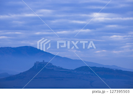 Spis Castle rising above the morning mist in blue hour with striped clouds 127395503