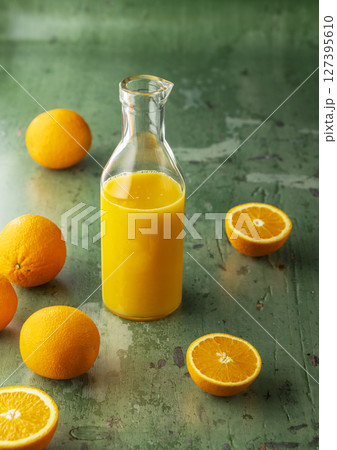 Refreshing orange juice in glass bottle surrounded by oranges on green background 127395610