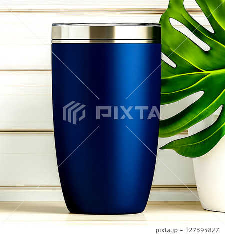 A blue tumbler sitting on top of a table next to a plant 127395827