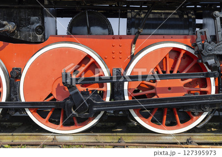 Red and black wheels of an old steam locomotive standing on rails 127395973