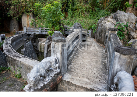 Rustic stone bridge with carved statues surrounded by lush greenery, Scenic pathway over a stone bridge with natural rock formations Rustic stone bridge with carved statues surrounded by lush greenery, Scenic pathway over a stone bridge with natural rock formations 127396221
