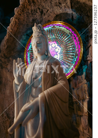 Illuminated Buddha statue with colorful halo in cave temple, Sacred Buddha sculpture with vibrant light in limestone cavern 127396237