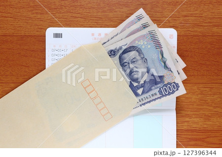 茶封筒に入れた千円札と預金通帳 127396344