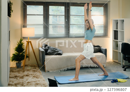Young woman practicing yoga in warrior pose on mat at home during morning workout Young woman practicing yoga in warrior pose on mat at home during morning workout 127396807