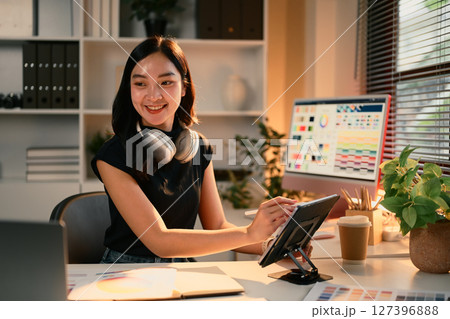 Cheerful graphic designer working on digital tablet in a creative studio with color palettes on screen 127396888