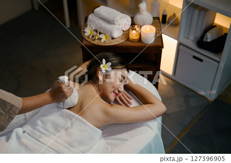 Young woman enjoying a relaxing herbal compress massage at a luxury spa. Wellness concept 127396905