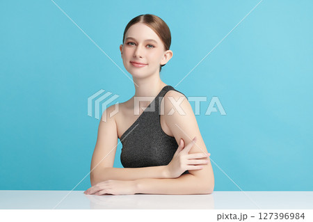 A beautiful young woman with clean, fresh skin against a blue background. Skincare, facial treatment, cosmetology, beauty, and spa. An elegant portrait of an woman. 127396984
