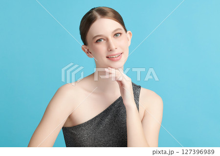 A beautiful young woman with clean, fresh skin against a blue background. Skincare, facial treatment, cosmetology, beauty, and spa. An elegant portrait of an woman. 127396989