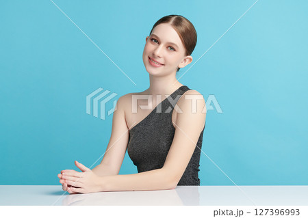A beautiful young woman with clean, fresh skin against a blue background. Skincare, facial treatment, cosmetology, beauty, and spa. An elegant portrait of an woman. 127396993