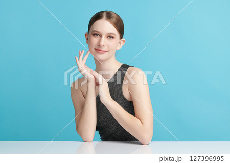 A beautiful young woman with clean, fresh skin against a blue background. Skincare, facial treatment, cosmetology, beauty, and spa. An elegant portrait of an woman. 127396995