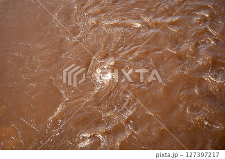 Close-Up of Muddy River Water Surface with Swirls and Reflections in Natural Light 127397217
