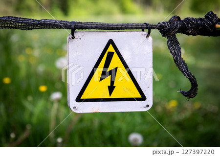 Warning Sign for Electrical Hazard Mounted on Fence with Green Field Background Warning Sign for Electrical Hazard Mounted on Fence with Green Field Background 127397220
