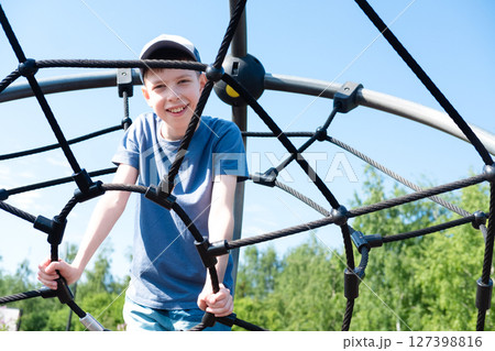 A teenage boy, 12 years old, wearing a cap and shorts, sits on the stairs at the top of the playground, smiles and looks at the camera A teenage boy, 12 years old, wearing a cap and shorts, sits on the stairs at the top of the playground, smiles and looks at the camera 127398816