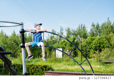 Teenage boy 12 years old in cap and shorts sitting on stairs at top of playground, side view Teenage boy 12 years old in cap and shorts sitting on stairs at top of playground, side view 127398817