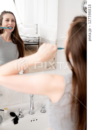 beautiful and young woman with braces, standing in front of the mirror in the bathroom and brushing her teeth beautiful and young woman with braces, standing in front of the mirror in the bathroom and brushing her teeth 127398818