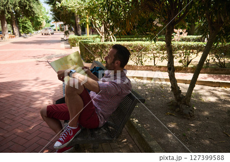 Man Relaxing on Park Bench Holding Map During Sunny Day Man Relaxing on Park Bench Holding Map During Sunny Day 127399588
