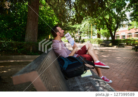 Man Relaxing on a Bench Reading a Newspaper in a Peaceful Park Man Relaxing on a Bench Reading a Newspaper in a Peaceful Park 127399589