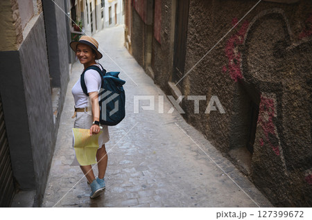 Young Woman Tourist Exploring a Historic European Alleyway with a Map and Backpack 127399672