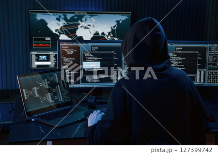 Dark room. Young professional female hacker is indoors by computer with lot of information on displays 127399742