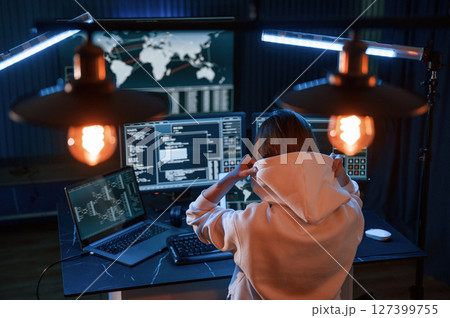 View from behind. Young professional female hacker is indoors by computer with lot of information on displays 127399755