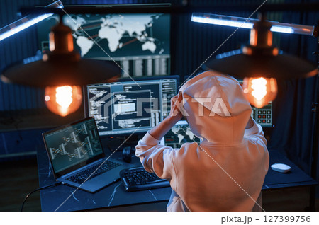 View from behind. Young professional female hacker is indoors by computer with lot of information on displays 127399756