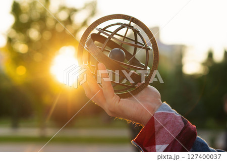 Hand holding antique metal globe against sunset in park Hand holding antique metal globe against sunset in park 127400037